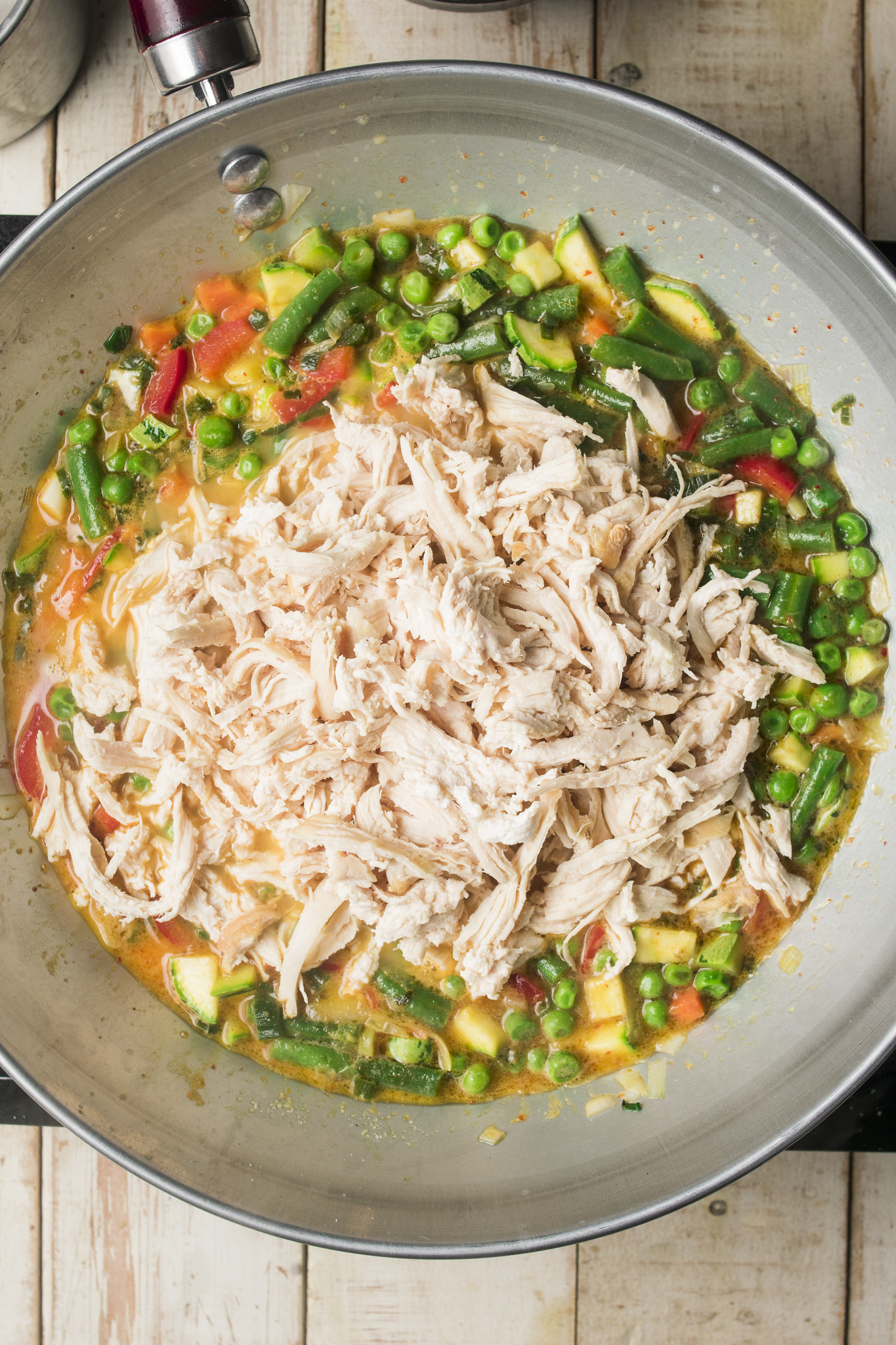 Shredded cooked chicken added to a Thai-inspired red curry with mixed vegetables in a wok.